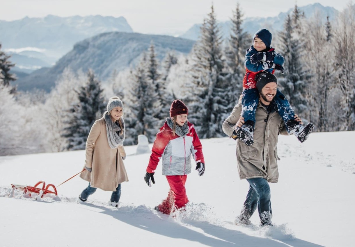 Eine Familie spaziert im Schnee, ein Kind auf den Schultern des Vaters