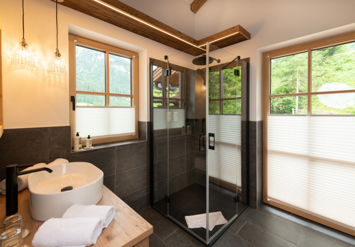 Modernes Badezimmer mit Eckdusche, Waschbecken und Blick ins Grüne durch zwei Fenster