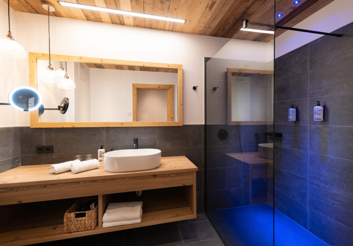 Modernes Badezimmer mit Holzdecke, blau beleuchteter Dusche und Waschtisch aus Holz