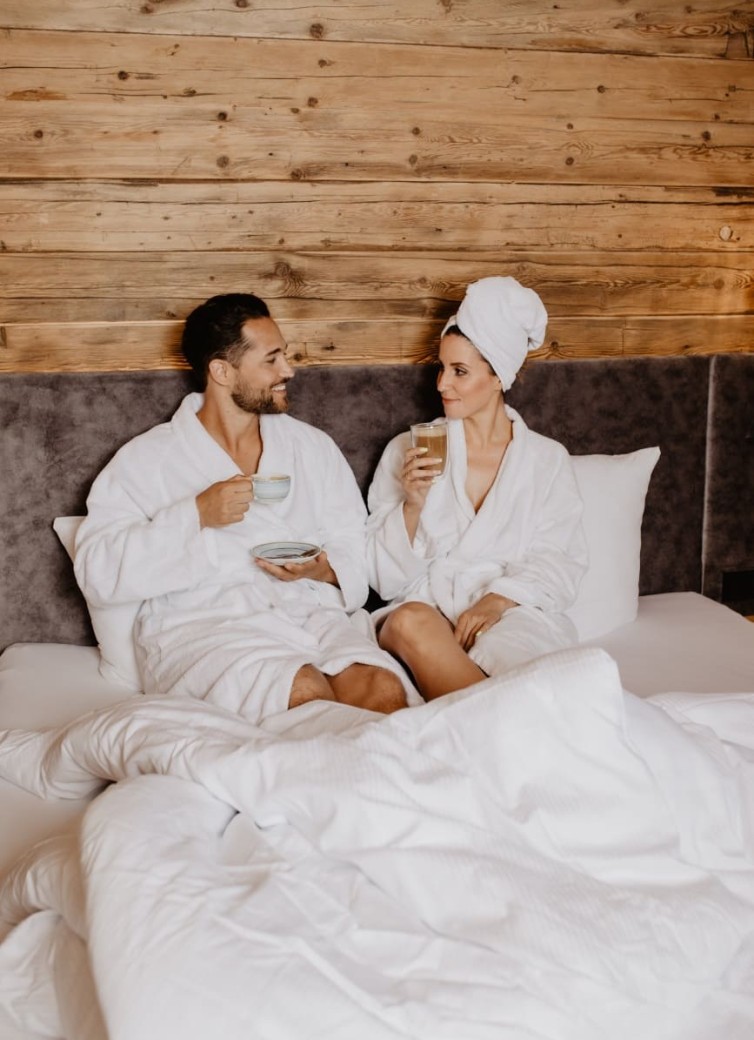 Ein Paar sitzt in Bademänteln im Bett und trinkt Kaffee