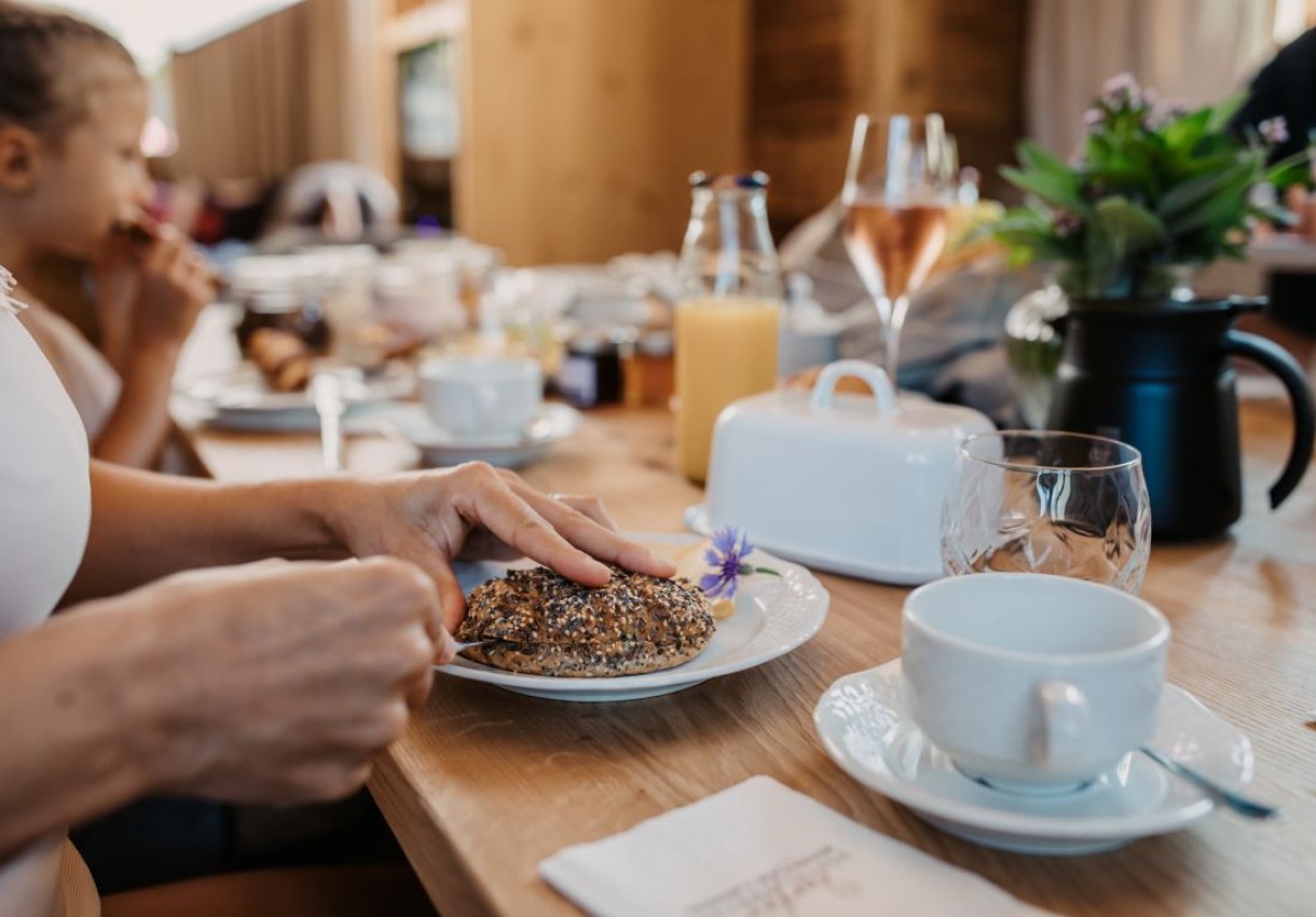 Person genießt ein Frühstück mit Brötchen und Getränken an einem Tisch