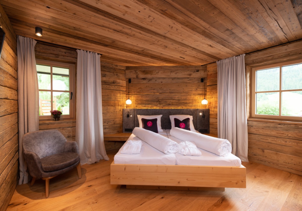 Rustikales Schlafzimmer mit Holzwänden, Doppelbett und Fenstern mit Vorhängen