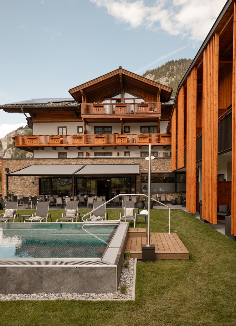 Hotel Dorfer mit Pool und Sonnenliegen im Garten vor einem bewaldeten Berghintergrund