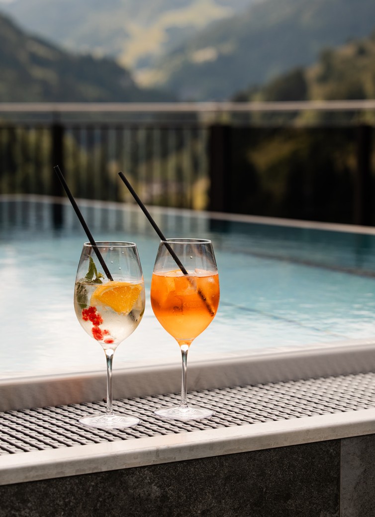 Zwei Getränke mit Strohhalmen am Pool vor Bergpanorama