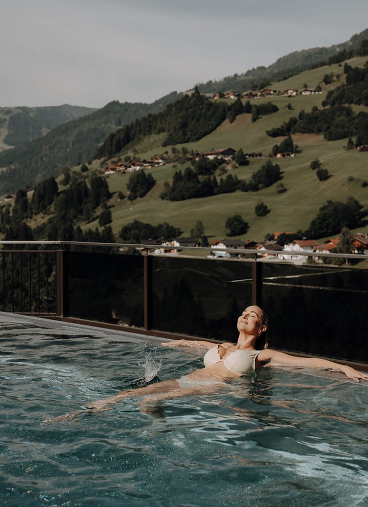 Eine Frau entspannt im Pool mit Blick auf eine gr&uuml;ne Berglandschaft