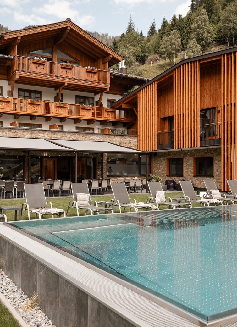 Hotel Dorfer mit Holzfassade und Pool, umgeben von Liegestühlen und Wald