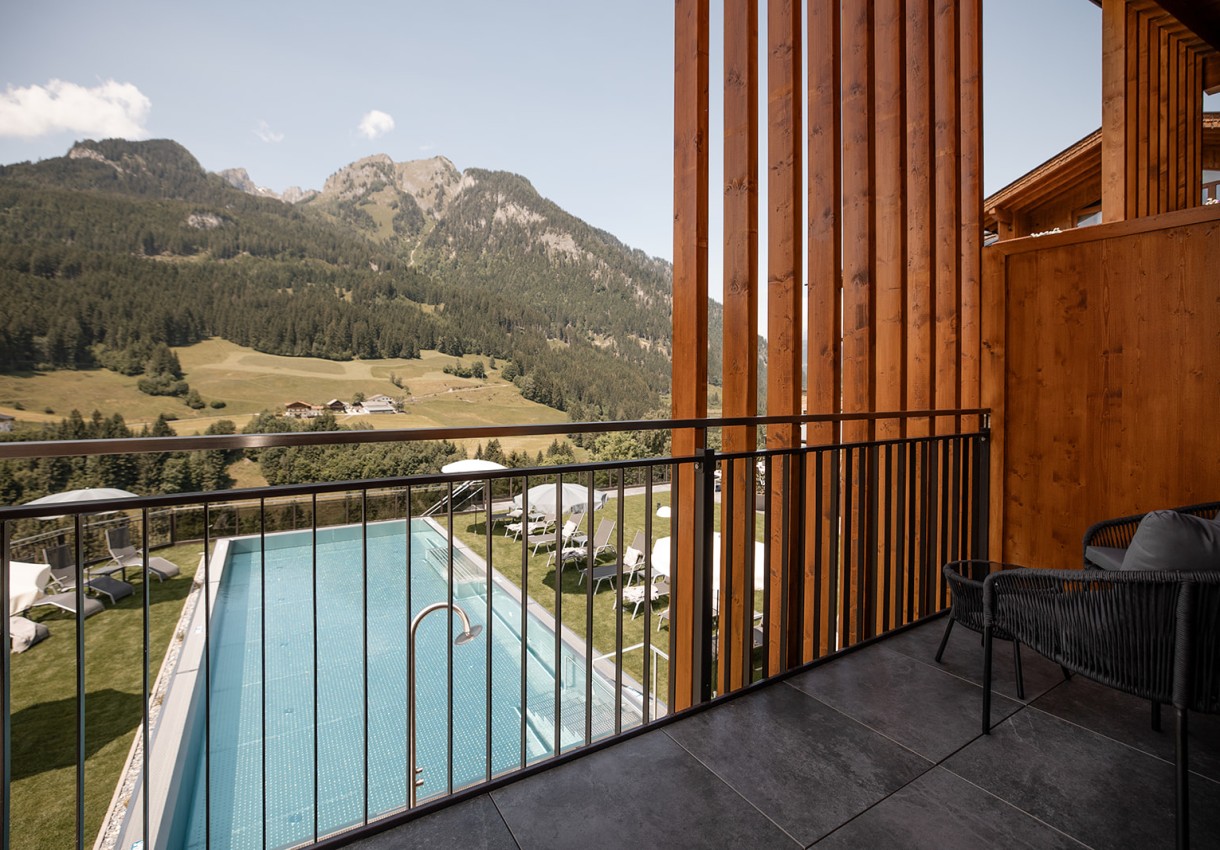 Blick von einer Terrasse auf einen Pool mit Berglandschaft im Hintergrund
