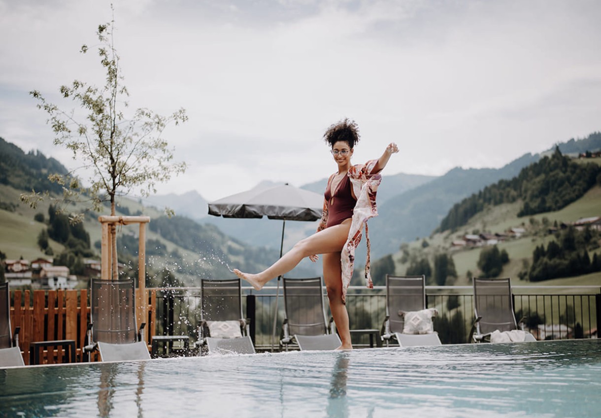 Frau genie&szlig;t die Zeit am Pool, im Hintergrund die malerische Bergkulisse