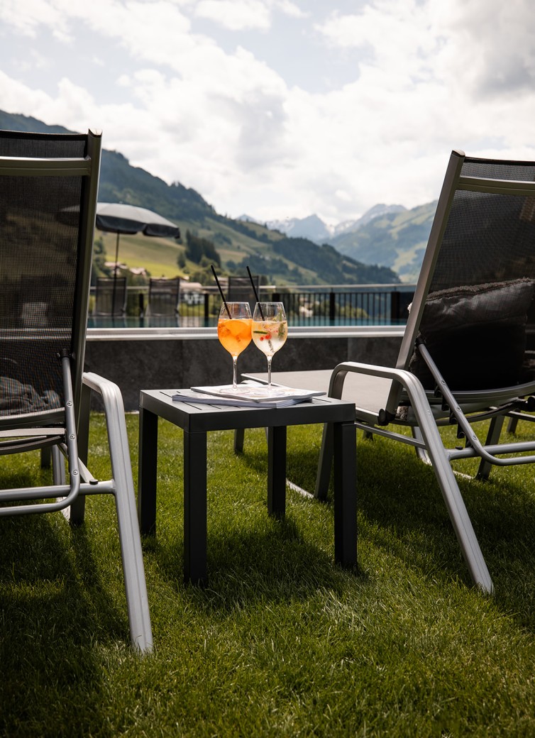 Zwei Getränke auf einem Tisch zwischen Liegestühlen mit Bergblick