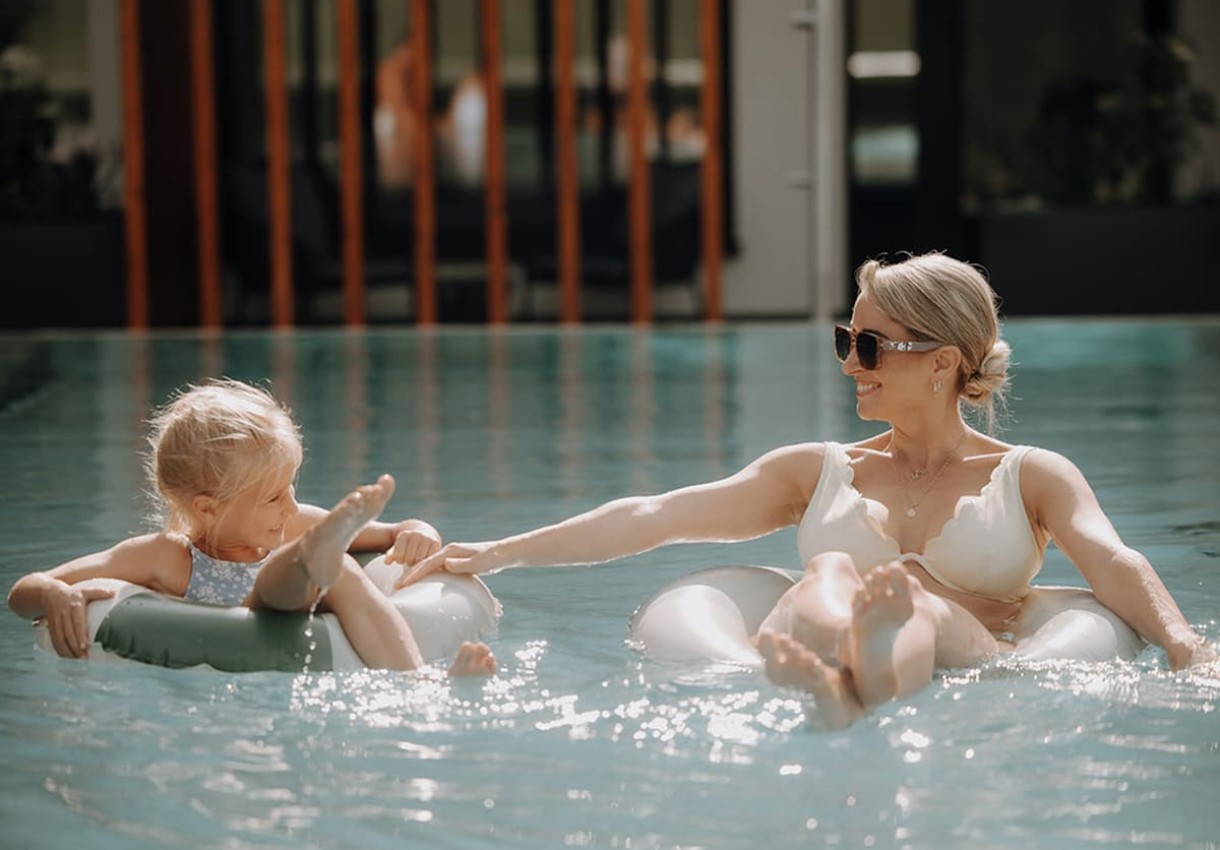 Mutter und Tochter entspannen sich lachend auf Schwimmreifen im Pool