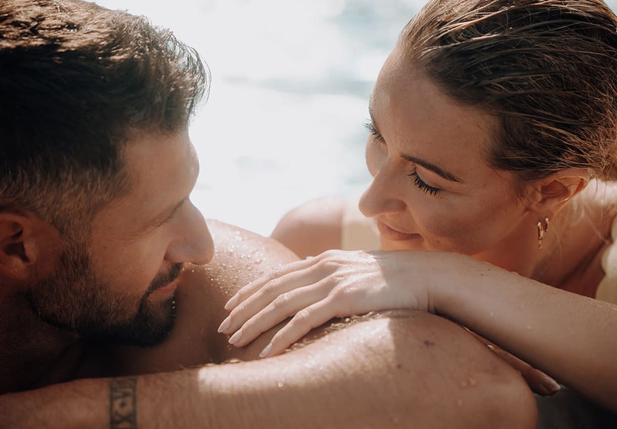 Paar liegt entspannt im Pool und schauen sich l&auml;chelnd an