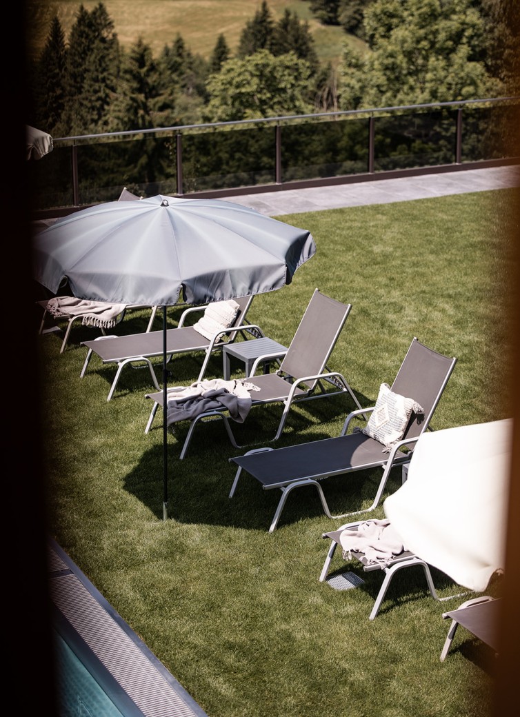 Sonnenliegen und Sonnenschirme stehen auf einer grünen Wiese neben einem Pool