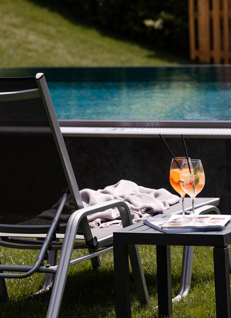 Liegestuhl am Pool mit Cocktails und Zeitschrift auf einem Tisch