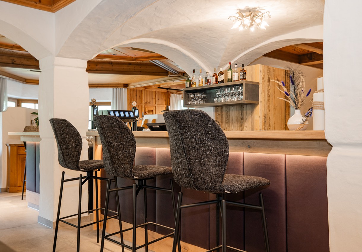 Eine stilvolle Bar mit hohen, gepolsterten Barhockern und Getränkeflaschen im Regal