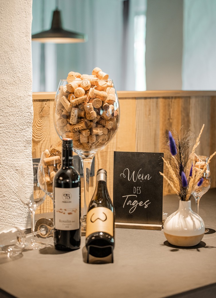 Zwei Weinflaschen und ein Schild mit "Wein des Tages" auf einem Tisch