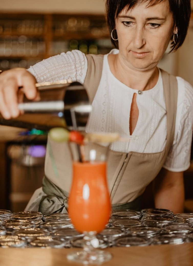 Eine Frau gießt ein Getränk aus einem Shaker in ein Glas mit rotem Cocktail