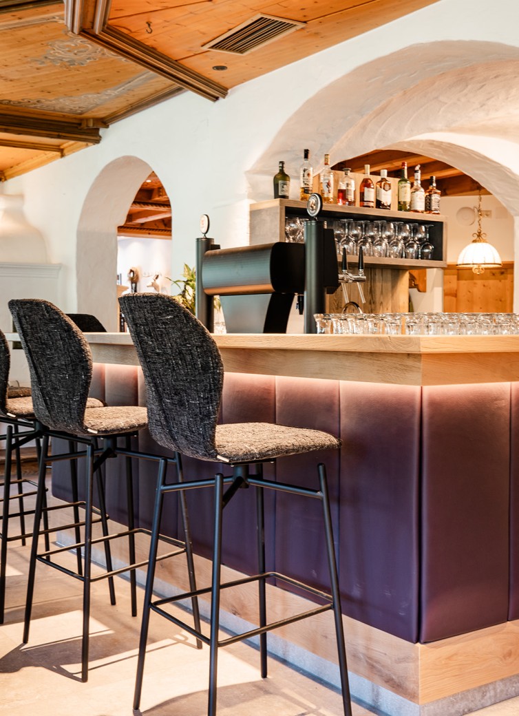 Bar mit hohen Stühlen und beleuchteter Theke, Gläser und Flaschen im Hintergrund