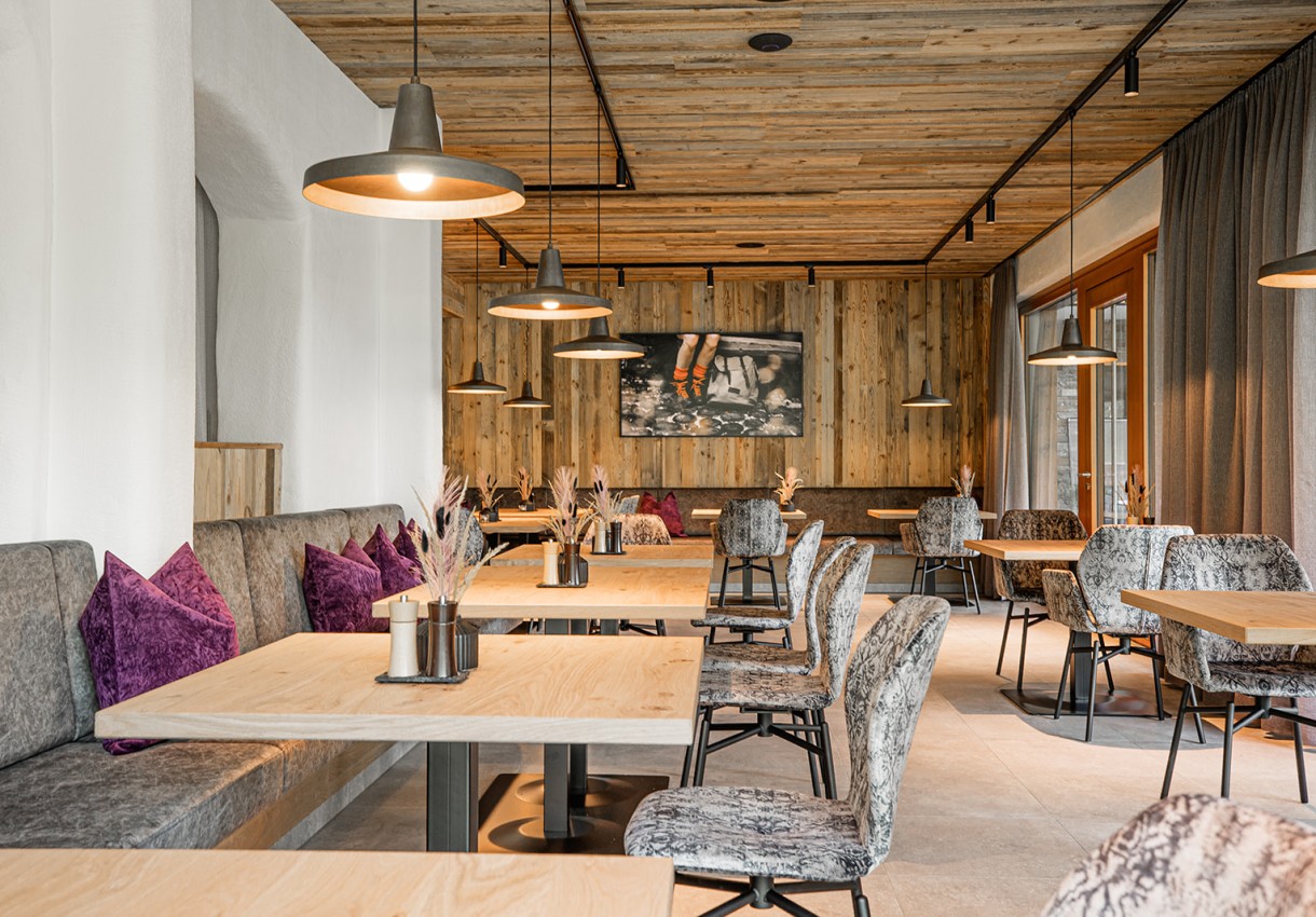 Gemütliches Restaurant mit Holzdekor, grauen Stühlen und lila Kissen auf den Sitzbänken