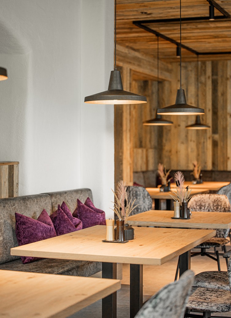 Gemütliches Café mit Holztischen, lila Kissen und hängenden Lampen