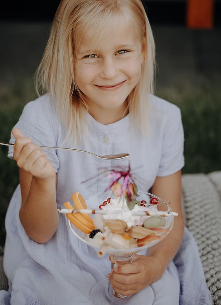 M&auml;dchen l&auml;chelt beim Essen ihres Eisbechers