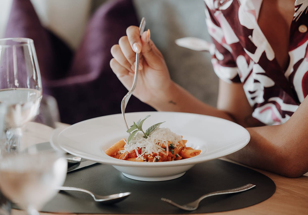 Person isst Pasta mit So&szlig;e und geriebenem K&auml;se im Restaurant Dorfer