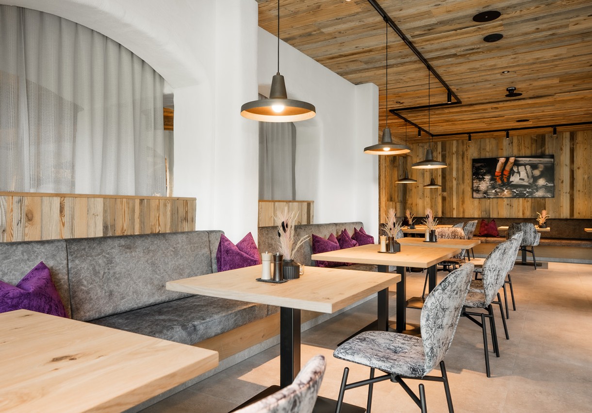 Restaurant vom Hotel Dorfer mit Holztischen, grauen Sitzbänken und lila Kissen