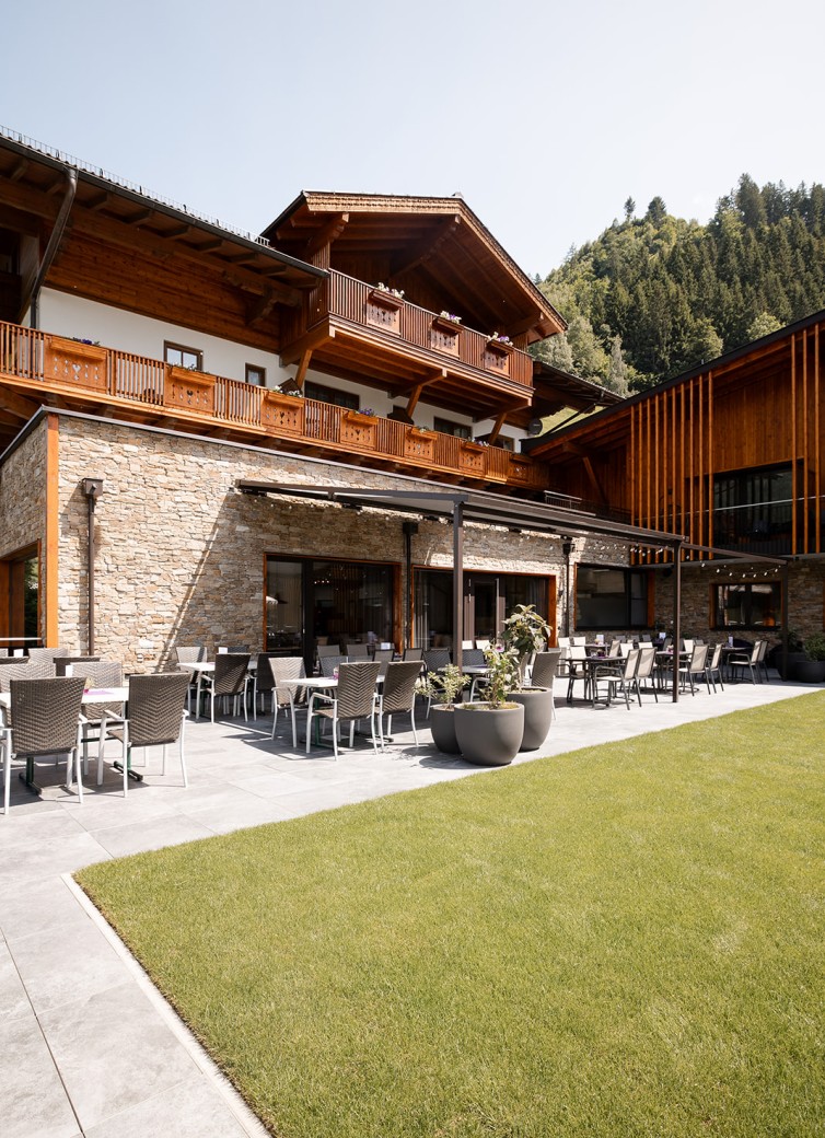 Hotel Dorfer mit Terrasse und Sitzbereich, umgeben von Wiese und Bäumen im Hintergrund