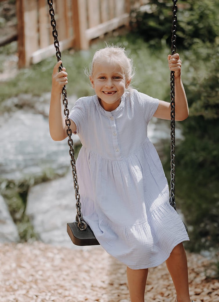 M&auml;dchen schaukelt am Dorfer Spielplatz und l&auml;chelt gl&uuml;cklich