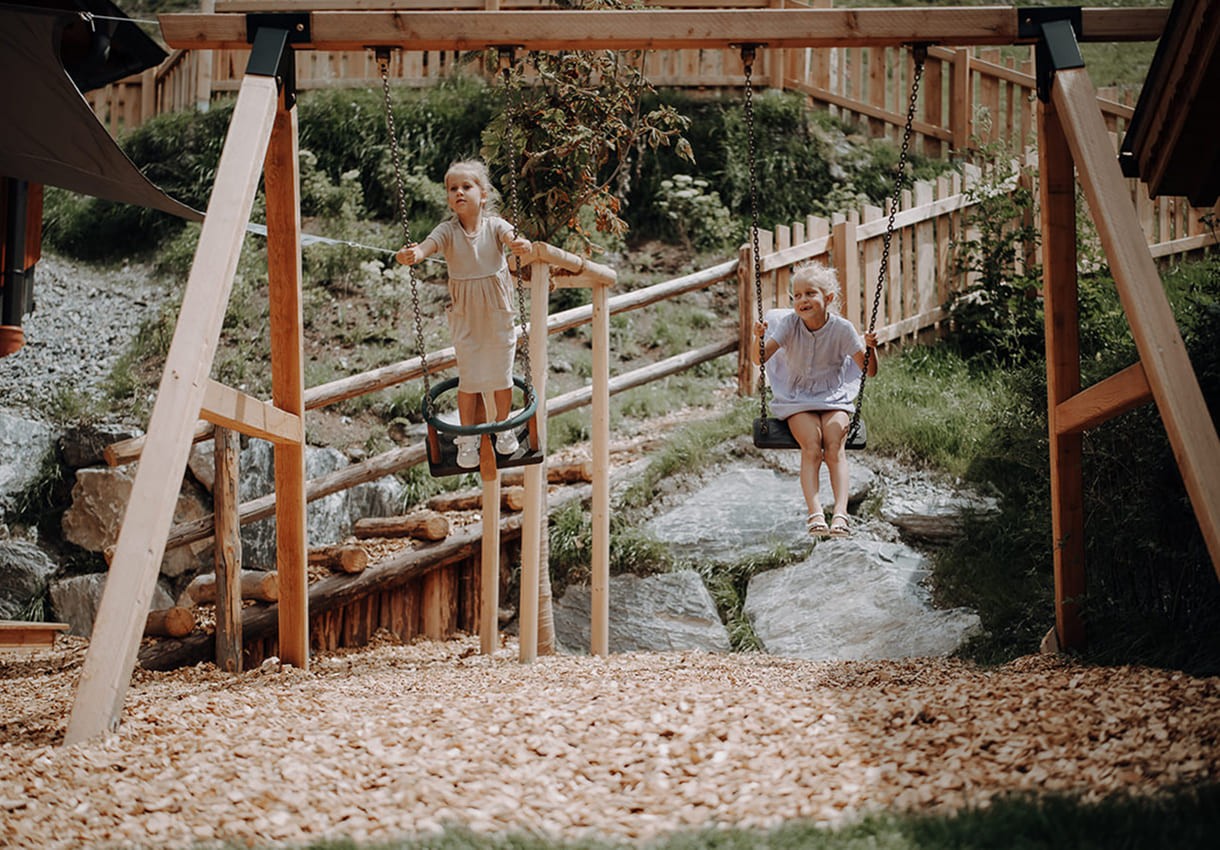 Zwei Kinder schaukeln drau&szlig;en auf einem Holzspielplatz