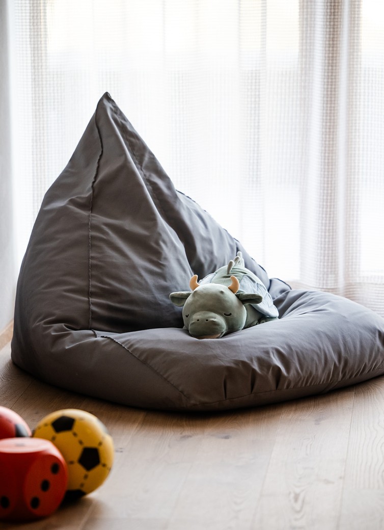 Grauer Sitzsack mit grünem Kuscheltier darauf, daneben bunte Spielwürfel und Bälle