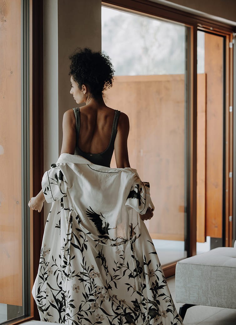 Eine Person steht am Fenster in einem Kleid mit Vogel- und Blumenmuster