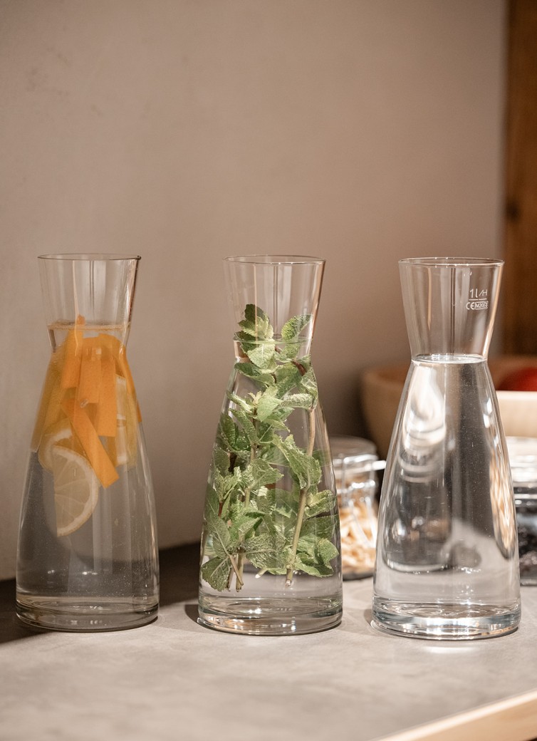Drei Glaskaraffen mit Wasser, eine mit Zitrone, eine mit Minze und eine ohne Zusätze