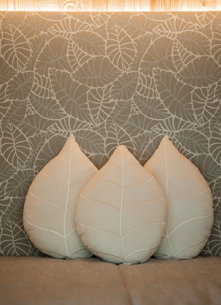 Drei blattförmige Kissen vor einer Wand mit Blattmuster darunter liegend