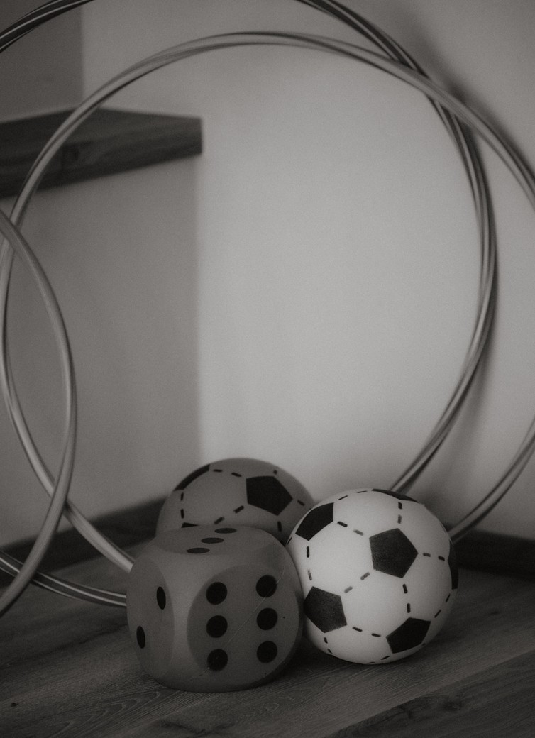 Drei Reifen, zwei Fußbälle und ein Würfel liegen auf einem Holzboden