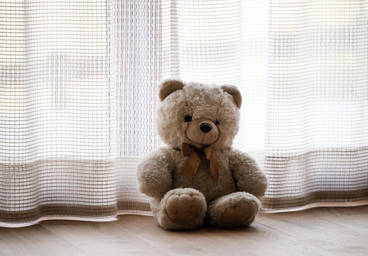 Ein Plüschbär sitzt vor weißen Vorhängen auf einem Holzboden