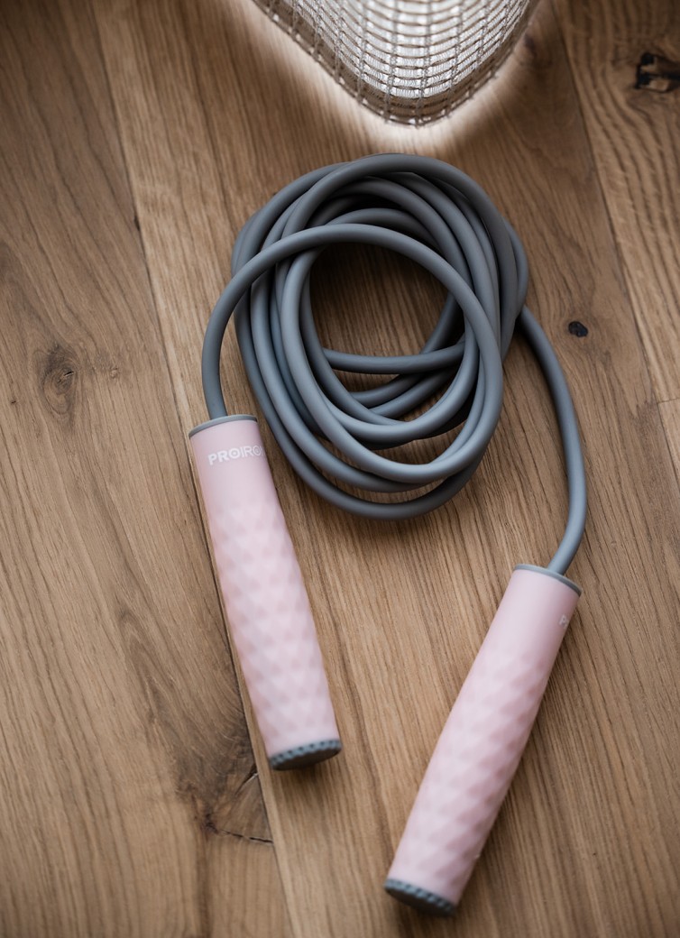 Springseil mit grauem Seil und rosa Griffen auf einem Holzboden