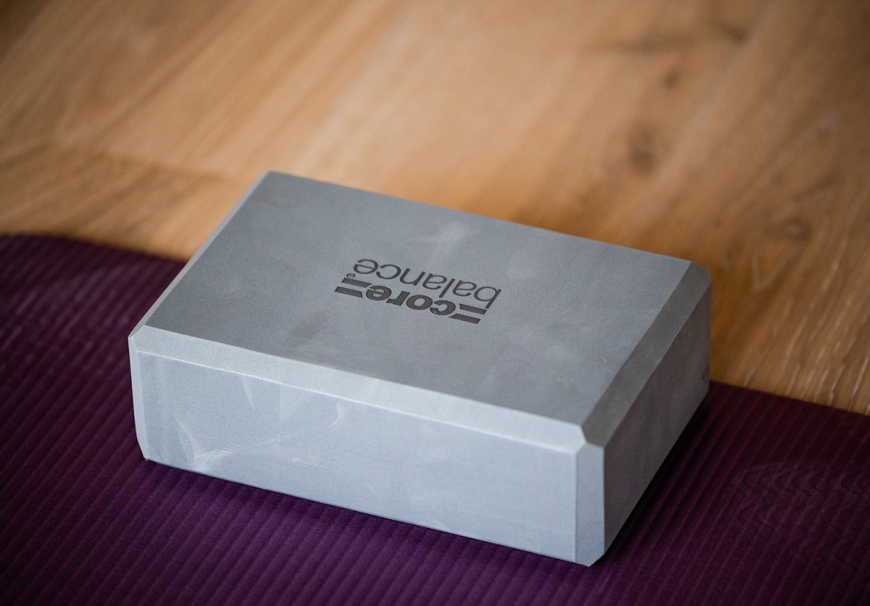 Grauer Yogablock liegt auf lila Yogamatte auf einem Holzboden