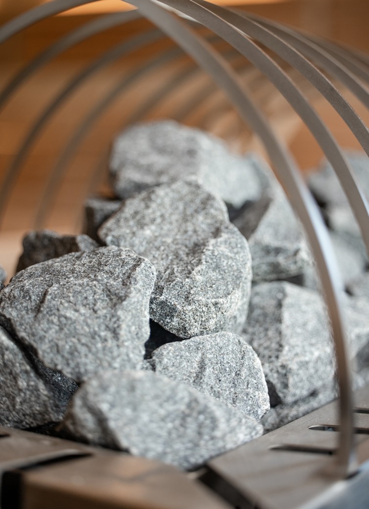Saunasteine auf einem Metallgitter, unscharfer Holzfond im Hintergrund