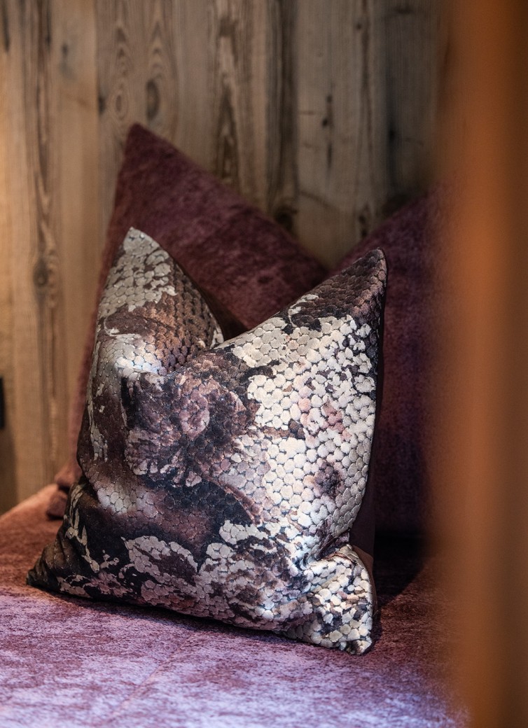 Ein gemustertes Kissen liegt auf einem violetten Sofa vor einer Holzwand