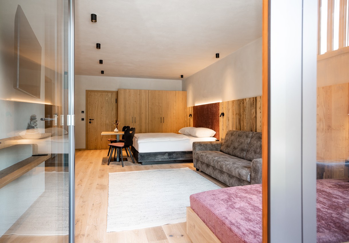 Modernes Hotelzimmer mit Holzvertäfelung, Doppelbett, Sofa und Esstisch