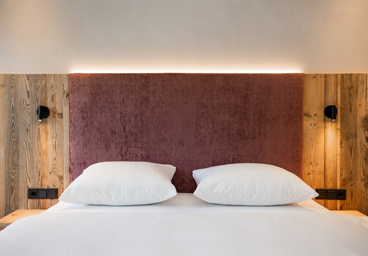 Modernes Doppelbett mit roten Kopfteilen und weißen Kissen, flankiert von Holz und Lampen