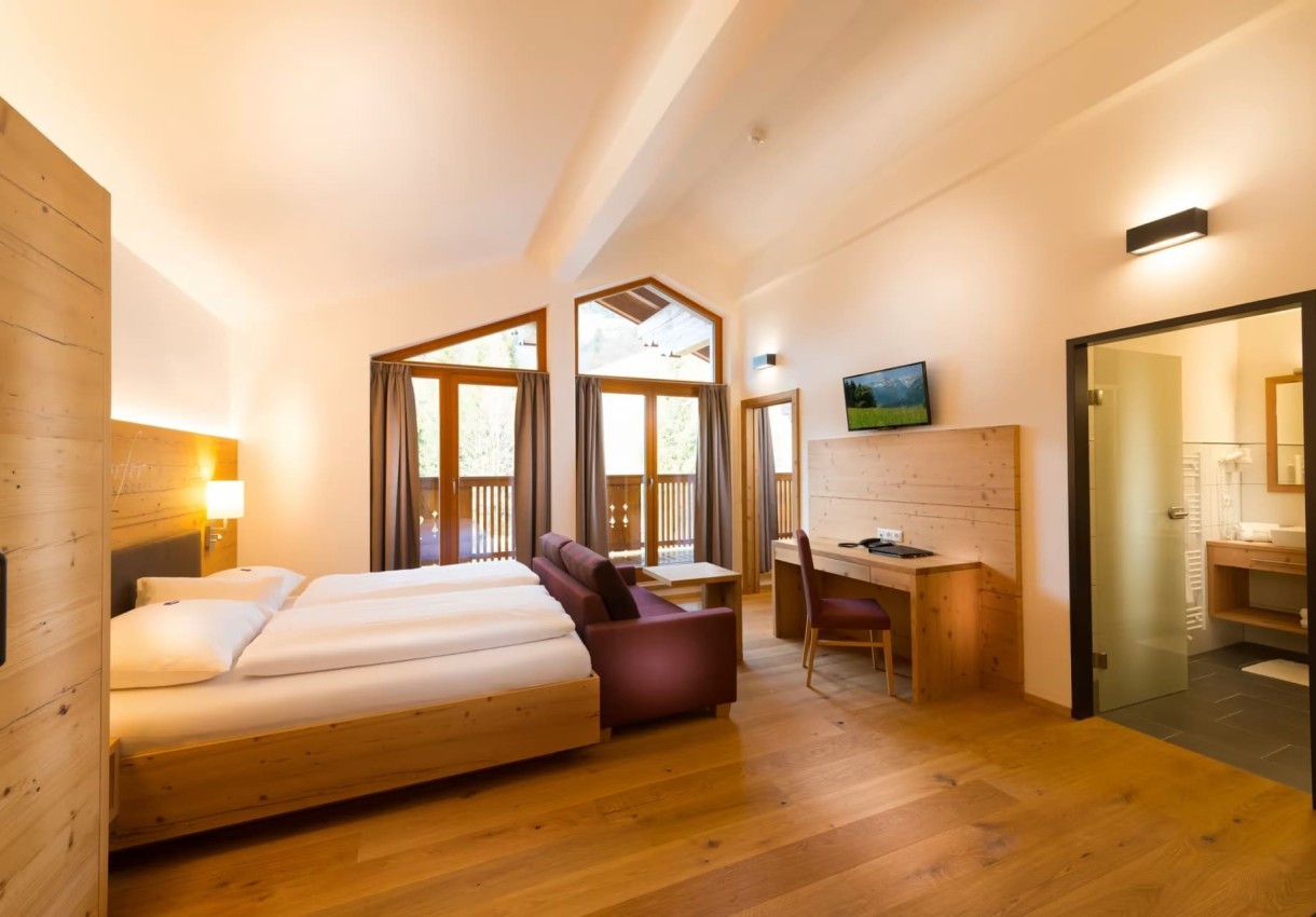 Zimmer im Hotel Dorfer mit Holzmöbeln, Balkon, Doppelbett, Schreibtisch und offener Badezimmertür