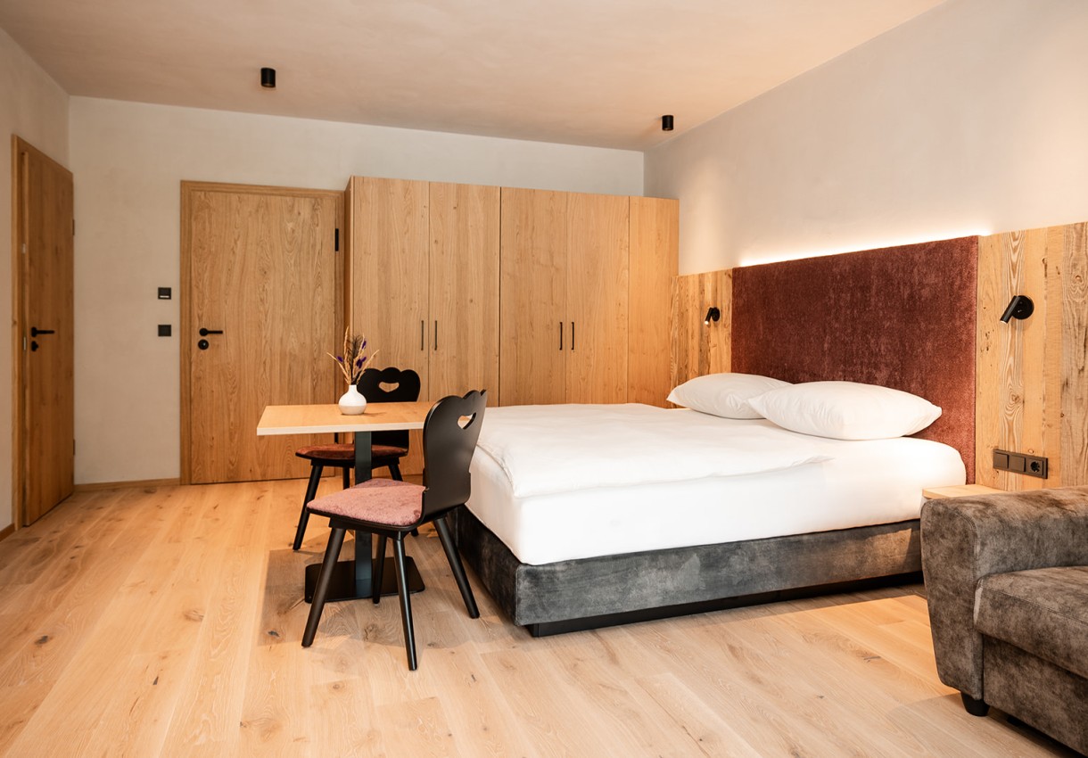 Helles Schlafzimmer mit Holzmöbeln, Doppelbett und kleinem Tisch mit Stühlen