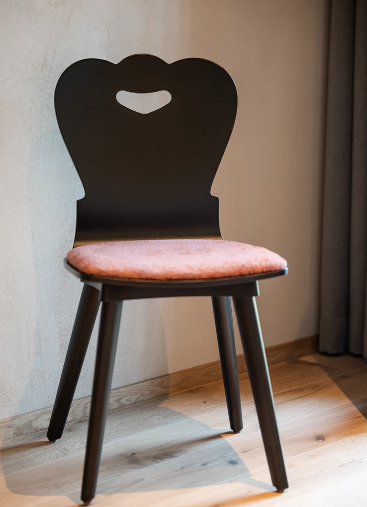 Schwarzer Stuhl mit herzförmiger Rückenlehne und gepolstertem Sitz vor einer Wand