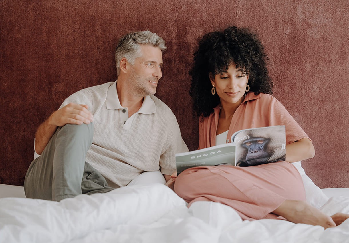 Paar sitzt entspannt auf dem Bett und liest ein Magazin
