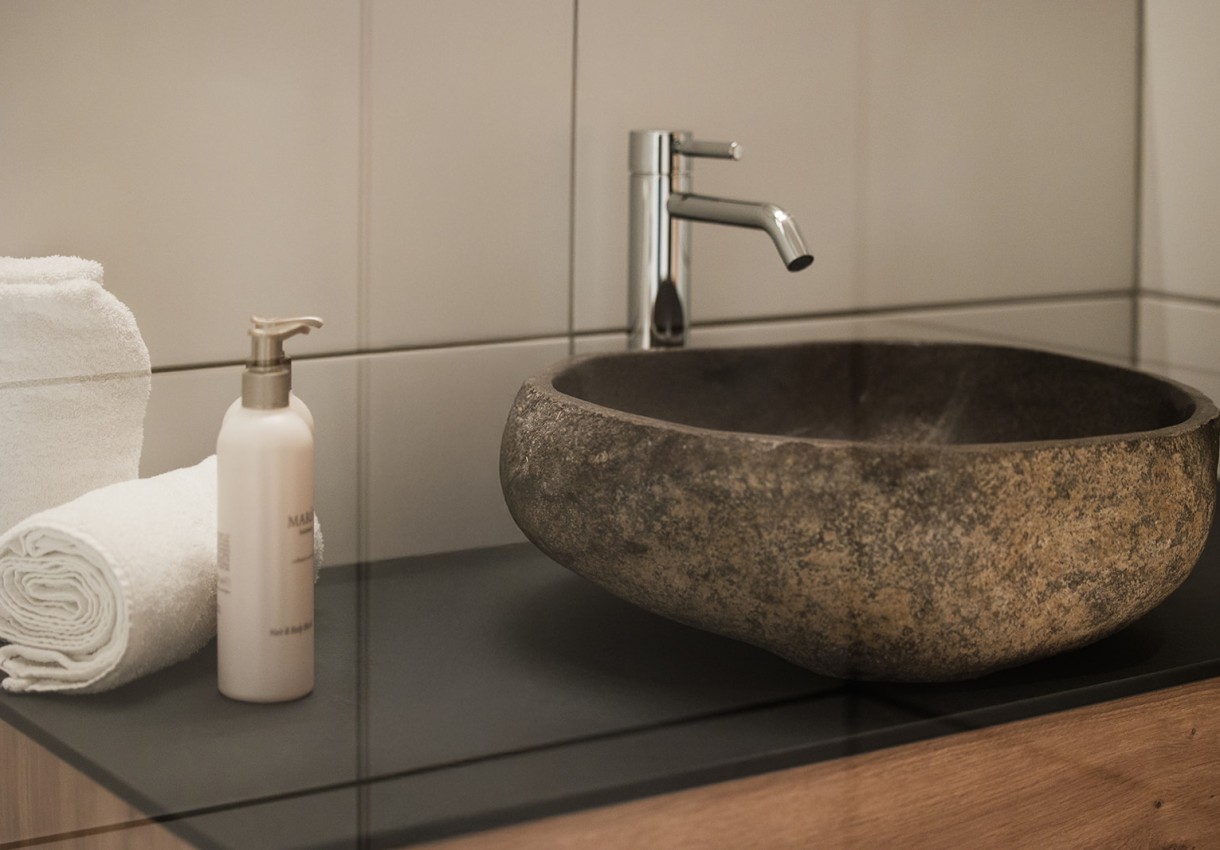 Steinwaschbecken mit Wasserhahn, daneben Handtücher und Lotionflasche