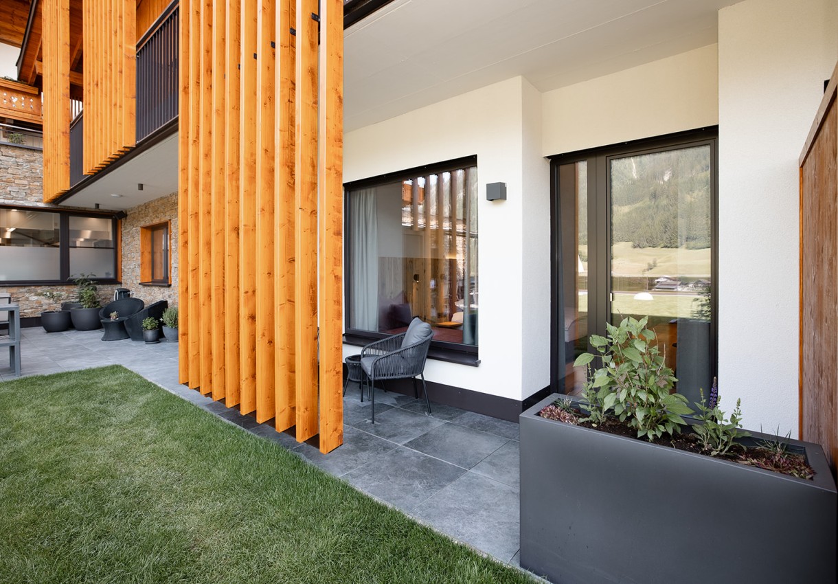 Moderner Balkon mit Holzlamellen, Glasfenstern, Rattanmöbeln und begrüntem Rasen