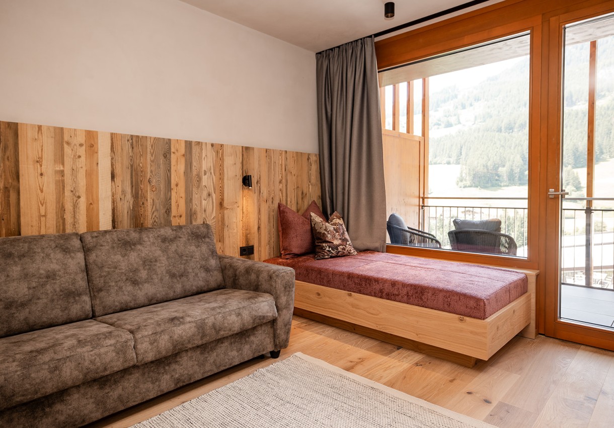 Gemütliches Wohnzimmer mit Sofa, Holzwand, Fensterfront und Blick auf die Landschaft