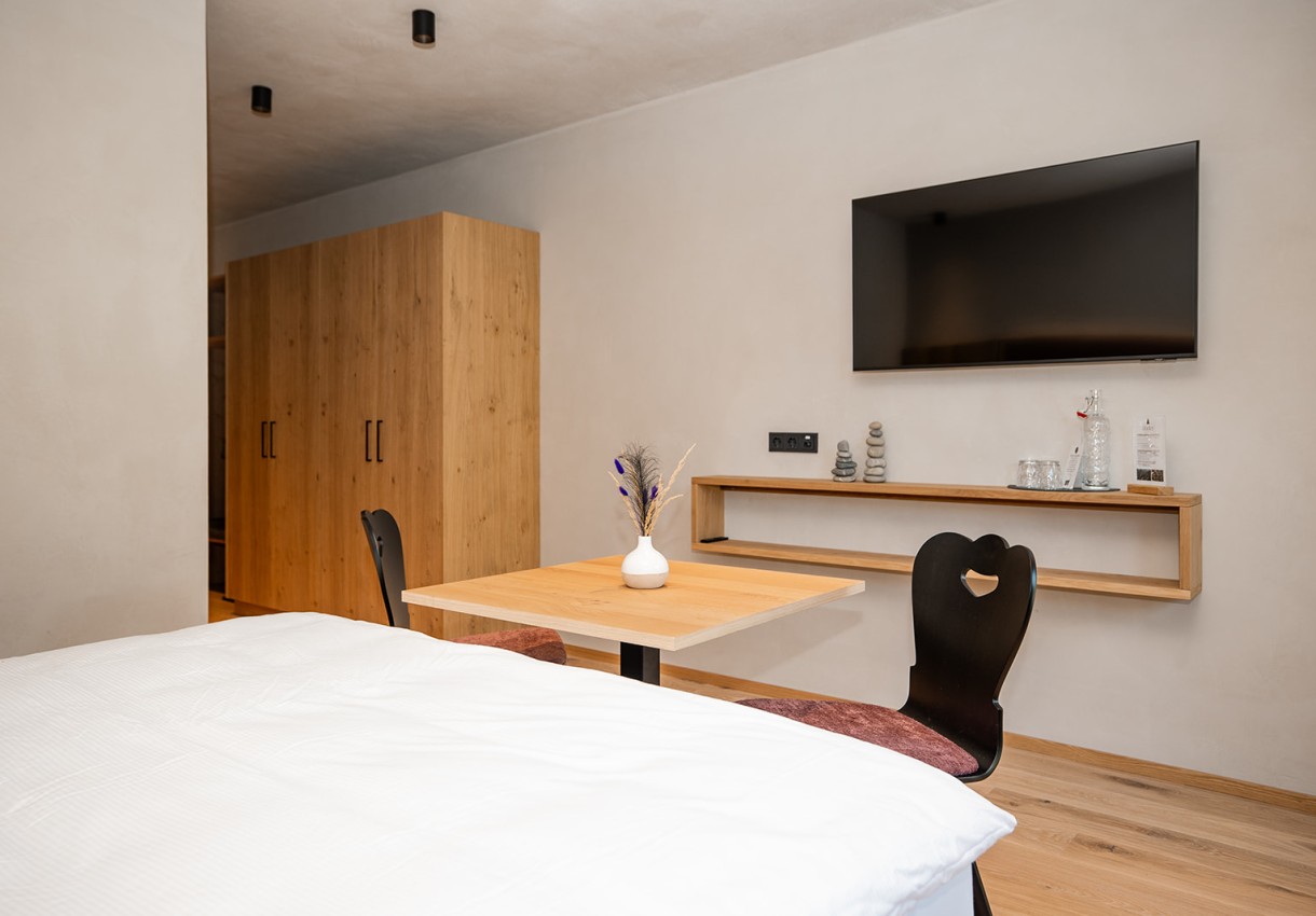 Helles Zimmer mit Holzmöbeln, einem Fernseher und einem kleinen Tisch mit zwei Stühlen