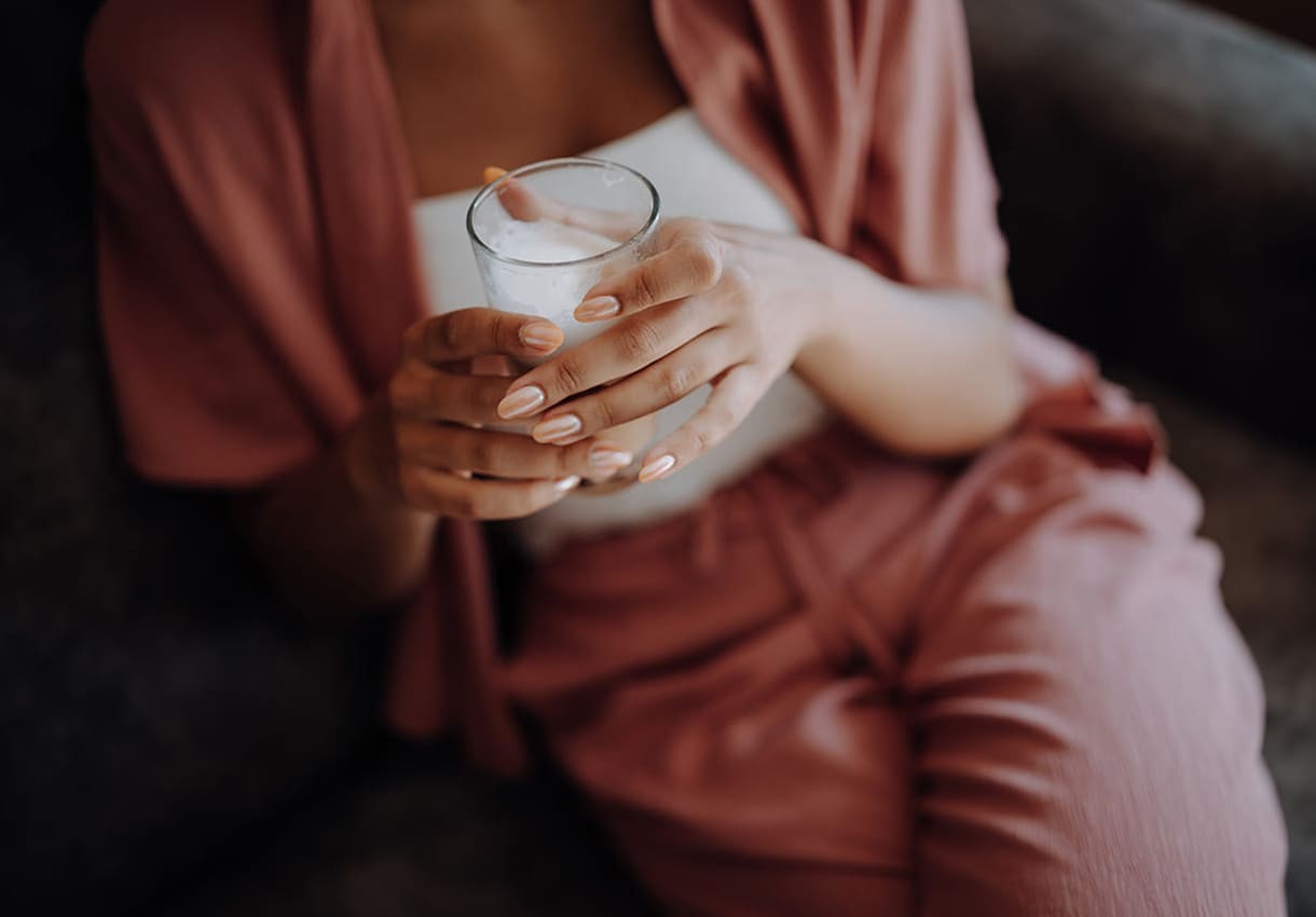 Frau entspannt mit einem Glas Wasser auf dem H&auml;ngesessel am Balkon ihres Zimmers